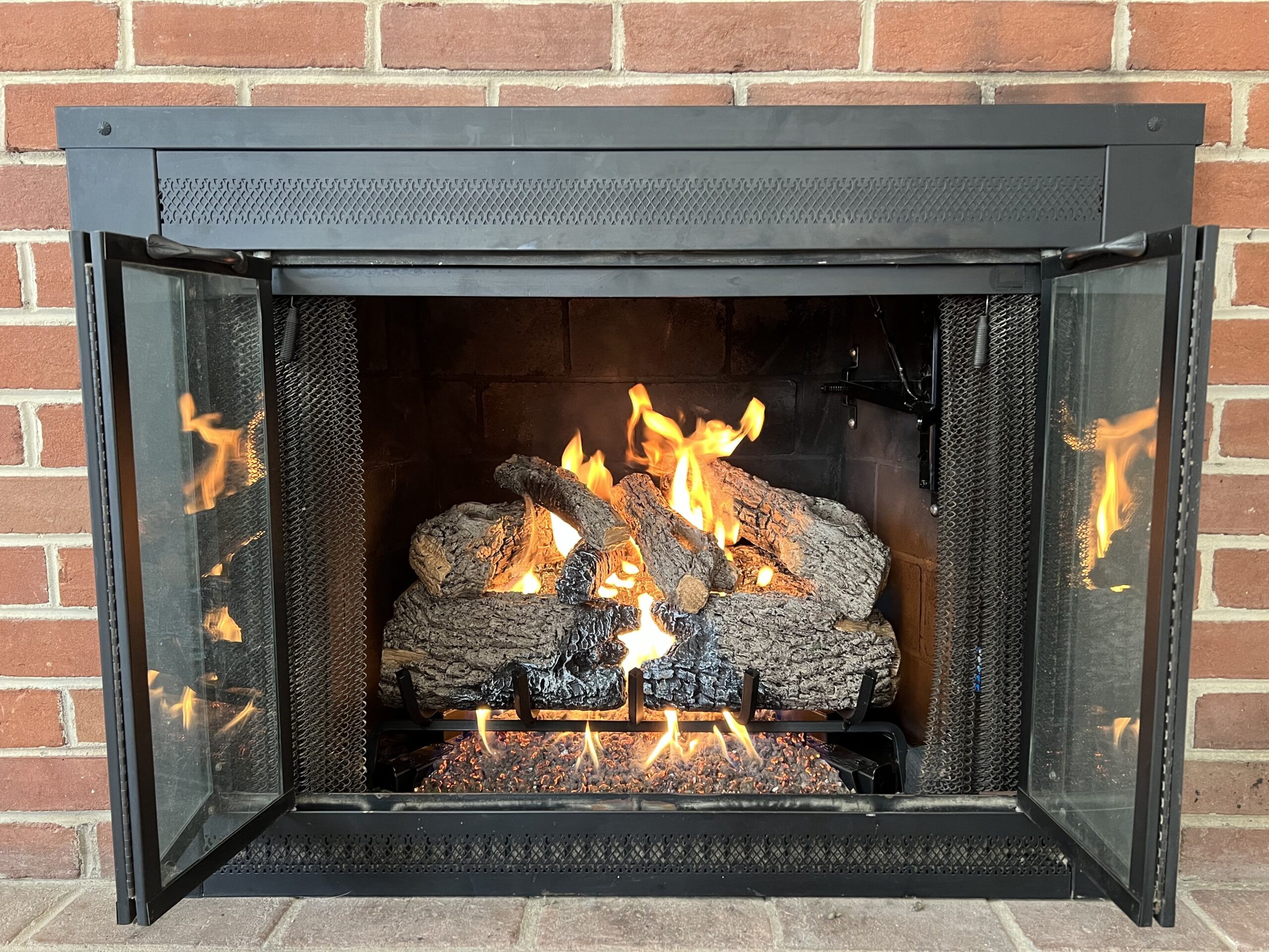 Vent less gas log set in a brick fireplace with open glass doors