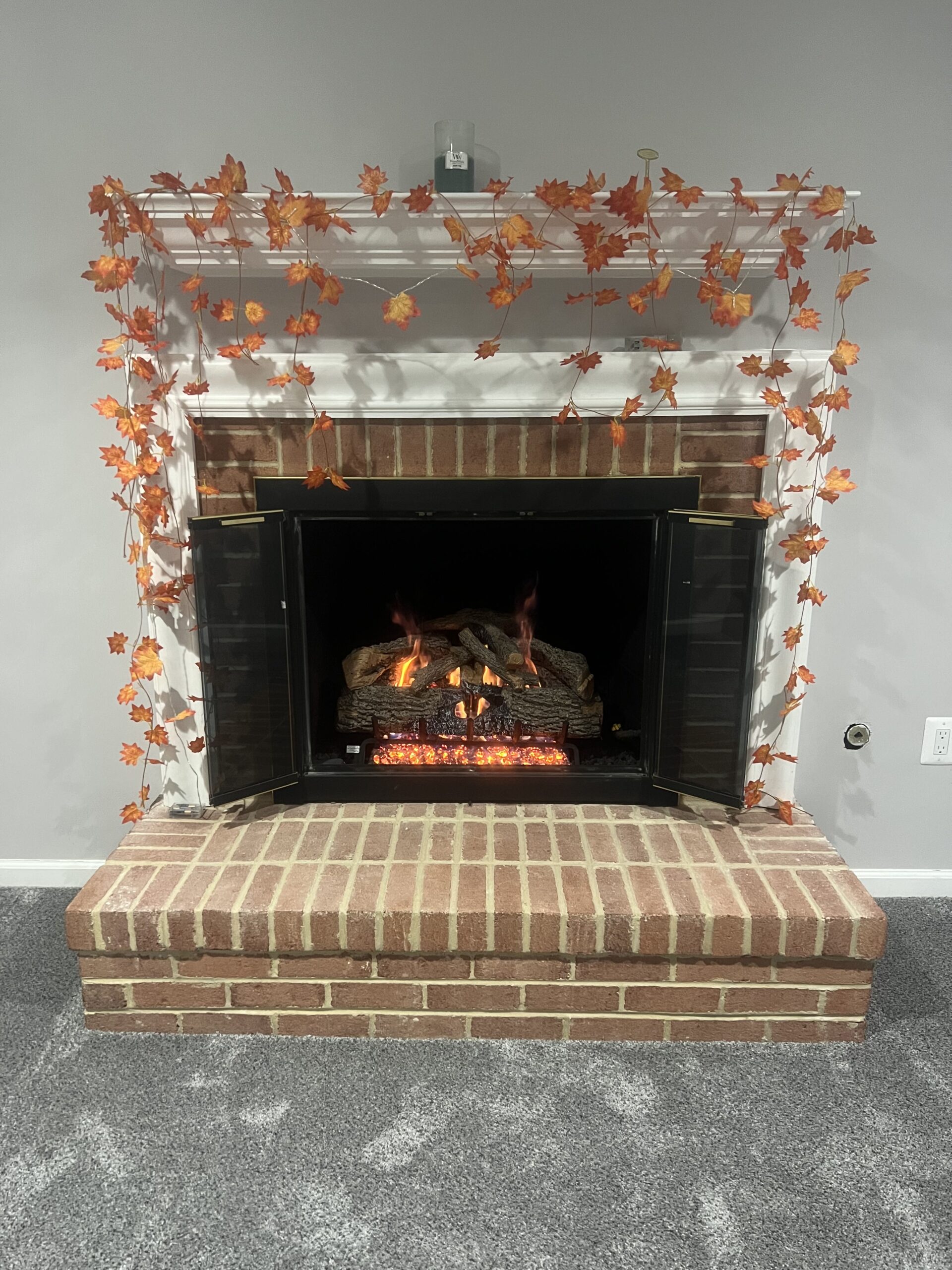 Gas fireplace log set with fall leaves around the mantel